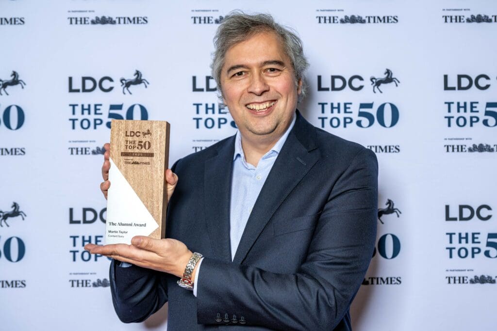 Martin Taylor, Co-Founder and Deputy CEO at Content Guru, stands with his 'Alumni Award' trophy against a sponsors wall at the The LDC Top 50 Most Ambitious Business Leaders Awards 2025.